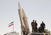 Silent Coup Rumors Rattle Tehran Military personnel standing near missile launchers with an Iranian flag in the background
