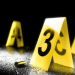 Yellow evidence markers with numbers at a crime scene alongside a bullet casing