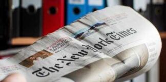 Newspaper held in hand with office binders in the background