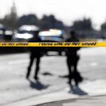 Police tape cordons off a street with patrol cars in the background