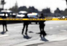 Police tape cordons off a street with patrol cars in the background
