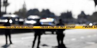 Police tape cordons off a street with patrol cars in the background