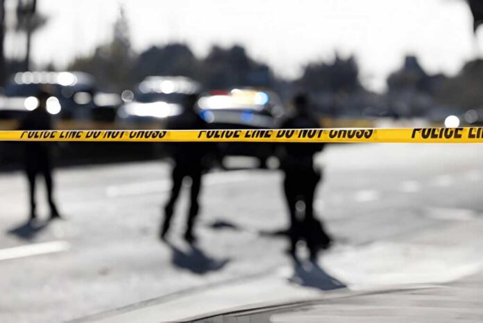 Police tape cordons off a street with patrol cars in the background