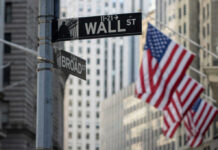 New York’s Biggest Risk Revealed Street signs for Wall Street and Broad Street with American flags in the background