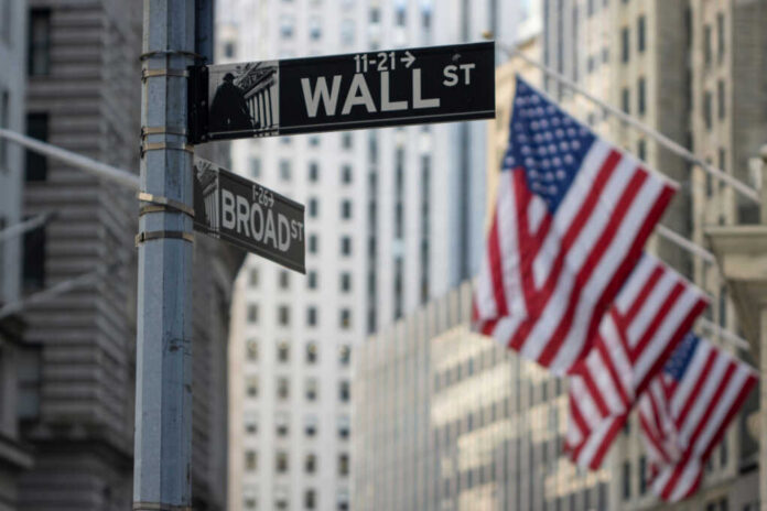 shutterstock2239853327jpg Street signs for Wall Street and Broad Street with American flags in the background