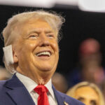A smiling man in a suit at a political rally, engaging with the audience