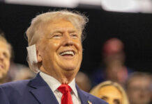 A smiling man in a suit at a political rally, engaging with the audience