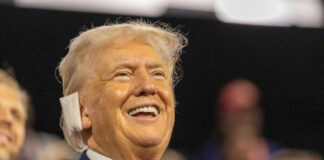 A smiling man in a suit at a political rally, engaging with the audience