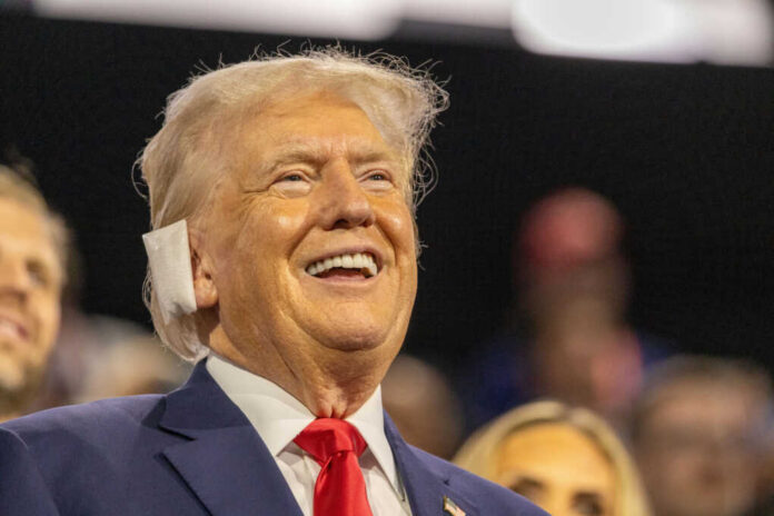 shutterstock2524665319jpg A smiling man in a suit at a political rally, engaging with the audience