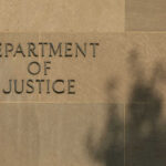 DOJ Sues Maryland Over Sanctuary Law Sign reading Department of Justice on a stone wall with a shadow