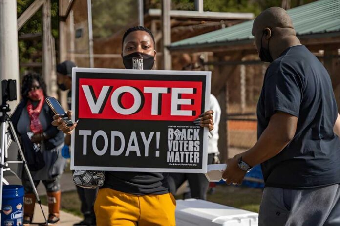 shutterstock_1885410739 Person holding a large voting sign at an outdoor event