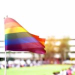 Girls’ Sports Ruling Sparks New Fight Rainbow flag waving in the foreground with a blurred crowd in the background
