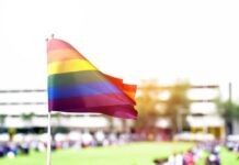 Girls’ Sports Ruling Sparks New Fight Rainbow flag waving in the foreground with a blurred crowd in the background