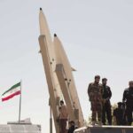 soldiers stand beside large missiles at outdoor display