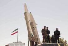 Iran Pays Price For Deadly Attack soldiers stand beside large missiles at outdoor display