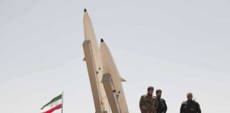 soldiers stand beside large missiles at outdoor display