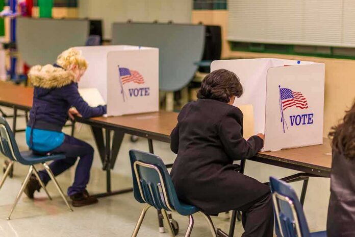shutterstock_1046168692 Voters seated at booths filling out ballots in a polling place