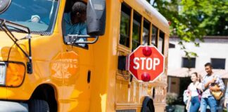 School bus with extended stop sign near students on sidewalk
