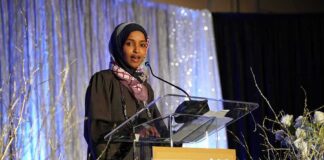 Woman in hijab speaking at a podium on a decorated stage
