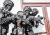 Warrant Hits Congressman Son’s Address Tactical officers in black gear stack up with rifles by a building