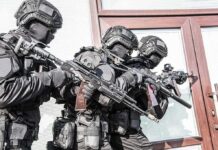 Tactical officers in black gear stack up with rifles by a building