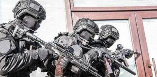 Tactical officers in black gear stack up with rifles by a building