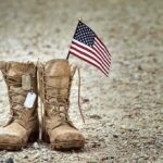 Combat boots with dog tags and a small American flag on gravel