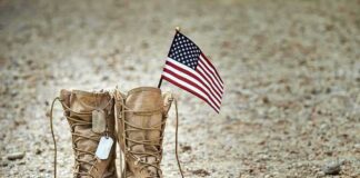 Combat boots with dog tags and a small American flag on gravel