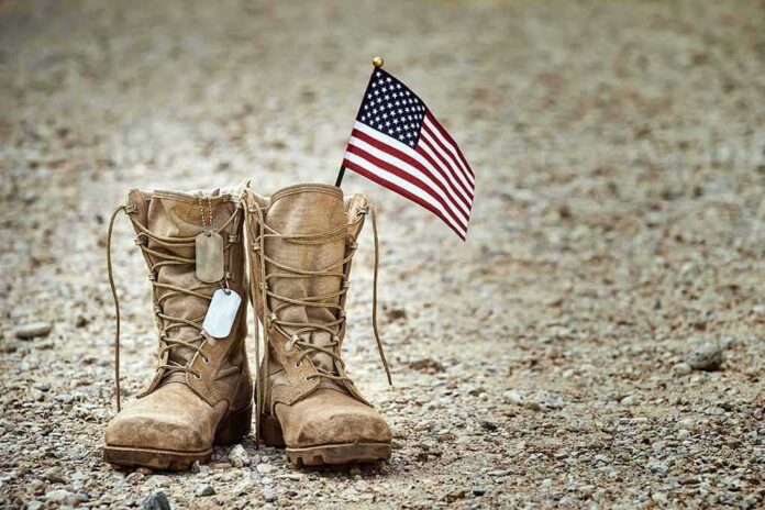 Combat boots with dog tags and a small American flag on gravel