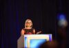 New Filing Brings Former Senator Into Spotlight Woman speaking at a podium on a stage