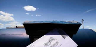 Mail-in ballot being inserted into a blue USPS mailbox