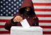 DOJ Bust Exposes Election-Immigration Trap Voter in hood and mask casting ballot into box
