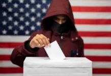 Voter in hood and mask casting ballot into box