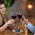 Two people clink red wine glasses at a restaurant table