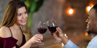 Two people clink red wine glasses at a restaurant table