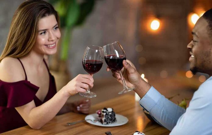 shutterstock_1921431176 Two people clink red wine glasses at a restaurant table