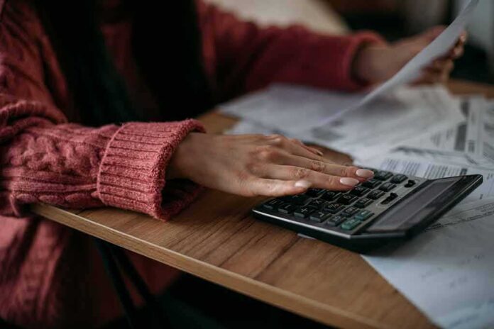 shutterstock_2140264515 Person using a calculator with bills on a desk