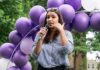 AOC’s Bold Move Rattles 2028 Field Woman speaking into a microphone at an outdoor event with purple balloons