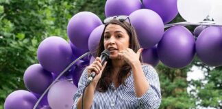 Woman speaking into a microphone at an outdoor event with purple balloons