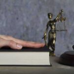 Washington Faces Trump’s Merit Test Hand on a book with gavel and Lady Justice statue