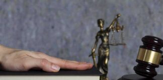 Hand on a book with gavel and Lady Justice statue