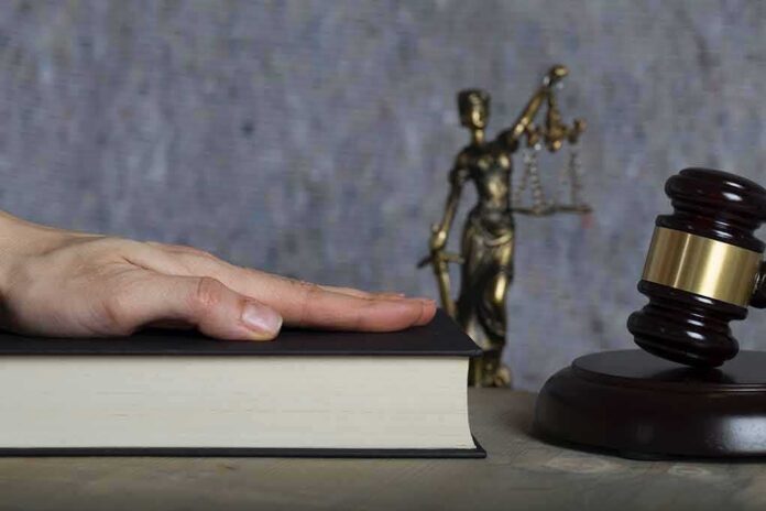 Hand on a book with gavel and Lady Justice statue