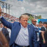 Rally Chaos Explodes In North Carolina Person in blue suit waving at outdoor event.