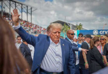 Rally Chaos Explodes In North Carolina Person in blue suit waving at outdoor event.