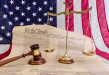 Scales of justice and gavel on the U.S. Constitution with American flag backdrop
