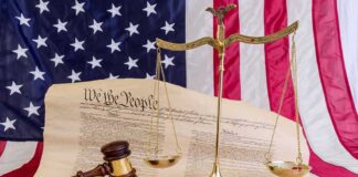 Scales of justice and gavel on the U.S. Constitution with American flag backdrop