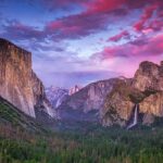 Granite cliffs and waterfall at sunset in a forested valley