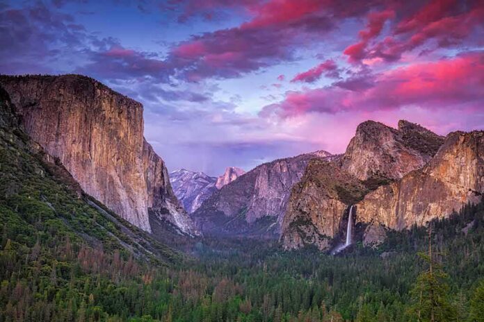 shutterstock_1130675216 Granite cliffs and waterfall at sunset in a forested valley