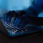 Hands typing on a backlit laptop keyboard at night