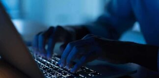Hands typing on a backlit laptop keyboard at night